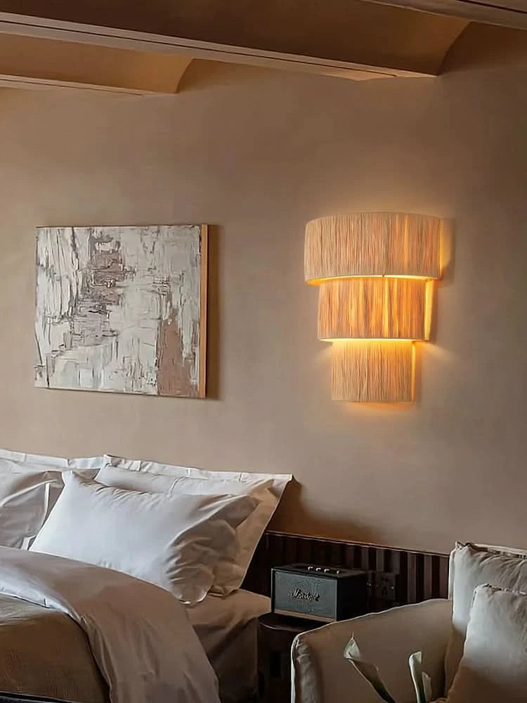 Natural raffia wall sconce light with warm glow illuminates a bedroom with artwork and bedding.
